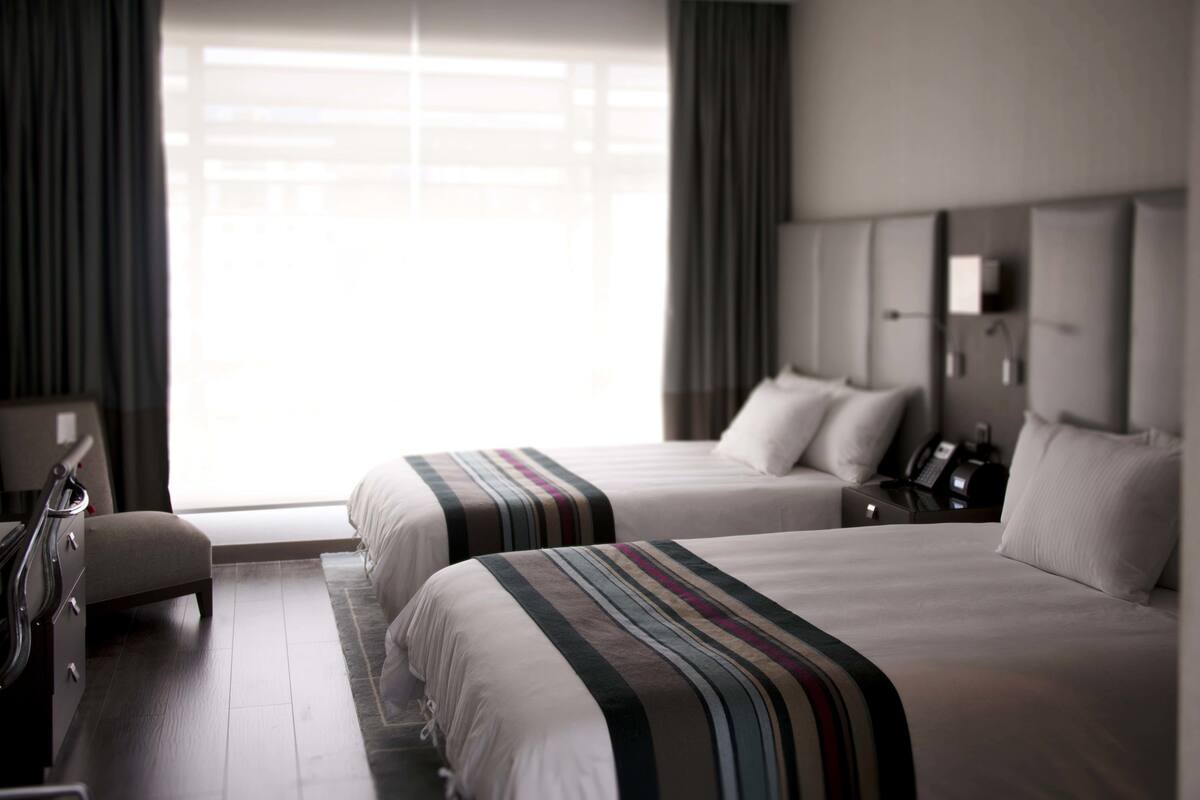 A hotel room with two beds, a desk, a chair, and a large window with curtains.