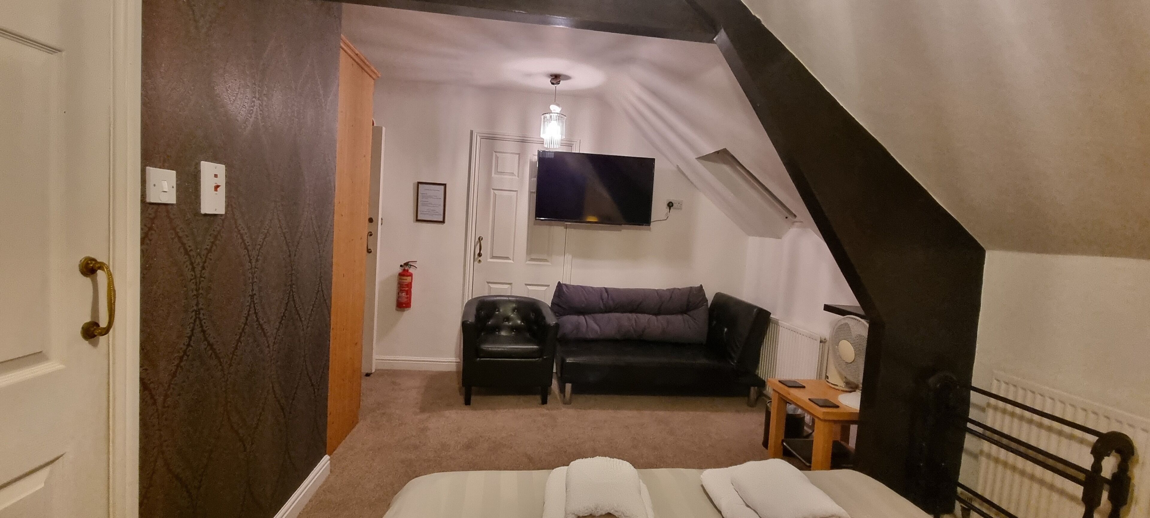 Ein kleiner, gemütlicher Raum mit einem Bett, einer schwarzen Ledersofa, einem an der Wand montierten Fernseher und einem Feuerlöscher.