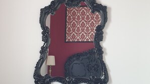 Una habitación con un escritorio de madera oscura, una silla con cojín rojo y un espejo grande y ornamentado con un fondo de diseño rojo y blanco.