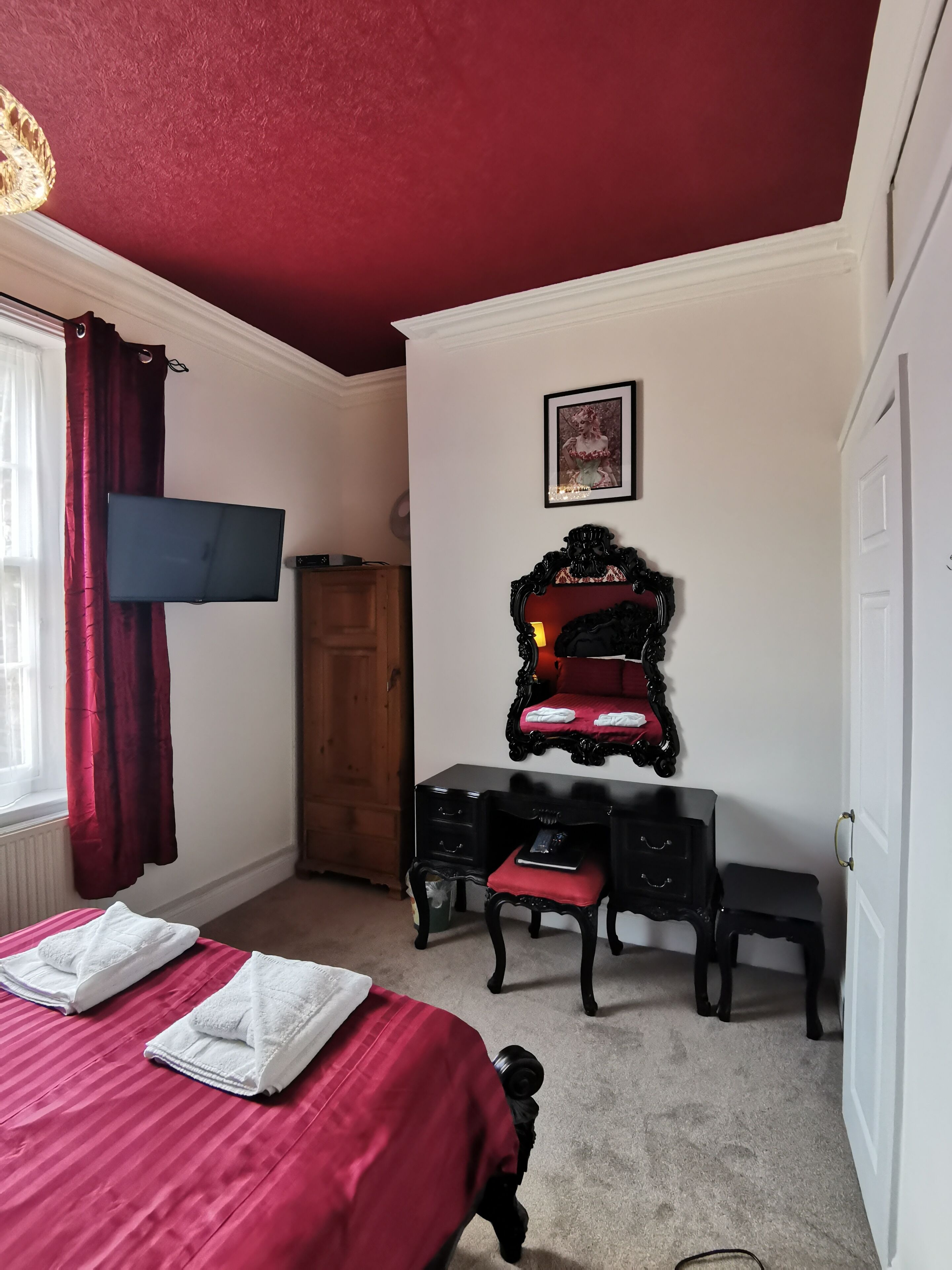 A bedroom with a bed, a desk, a chair, a wardrobe, and a framed picture on the wall.