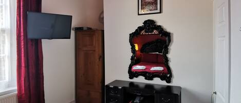 A bedroom with a bed, a desk, a chair, a wardrobe, and a framed picture on the wall.