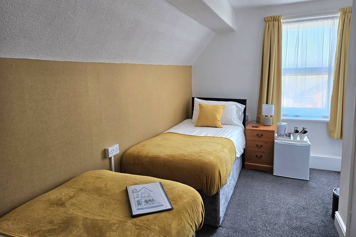 Una habitación de hotel con dos camas, una mesita de noche, una lámpara y una ventana con cortinas.