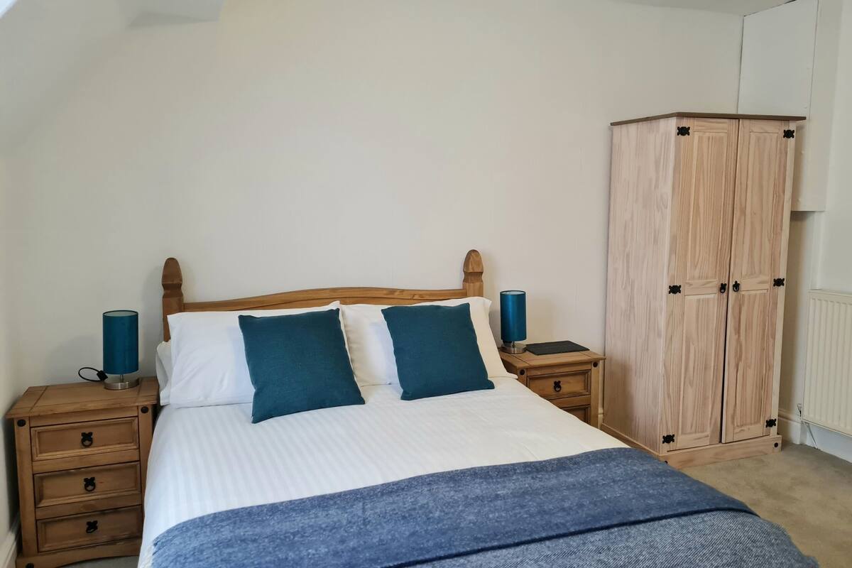 Un dormitorio con una cama de madera, dos mesitas de noche con lámparas, un armario y un radiador.