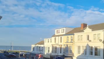 A coastal street with white buildings, a visible hotel, and parked cars.