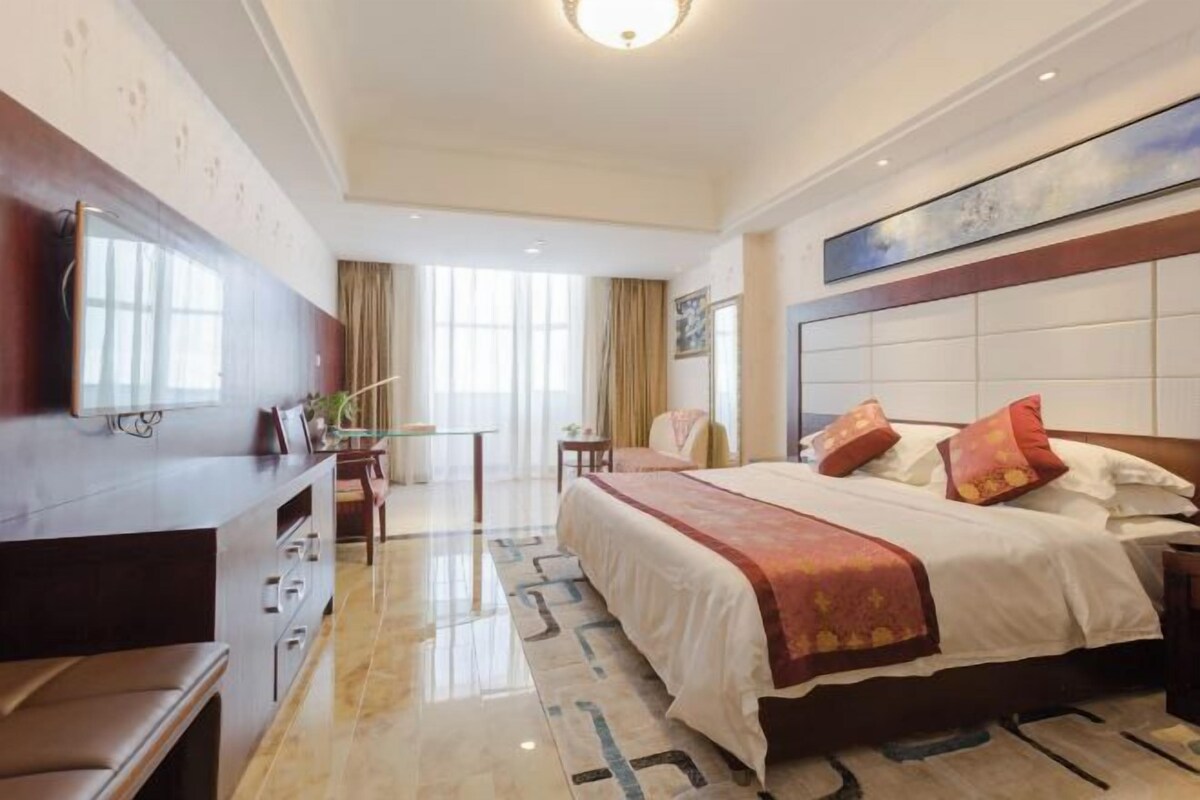 A hotel room with a large bed, a desk, a chair, and a television.