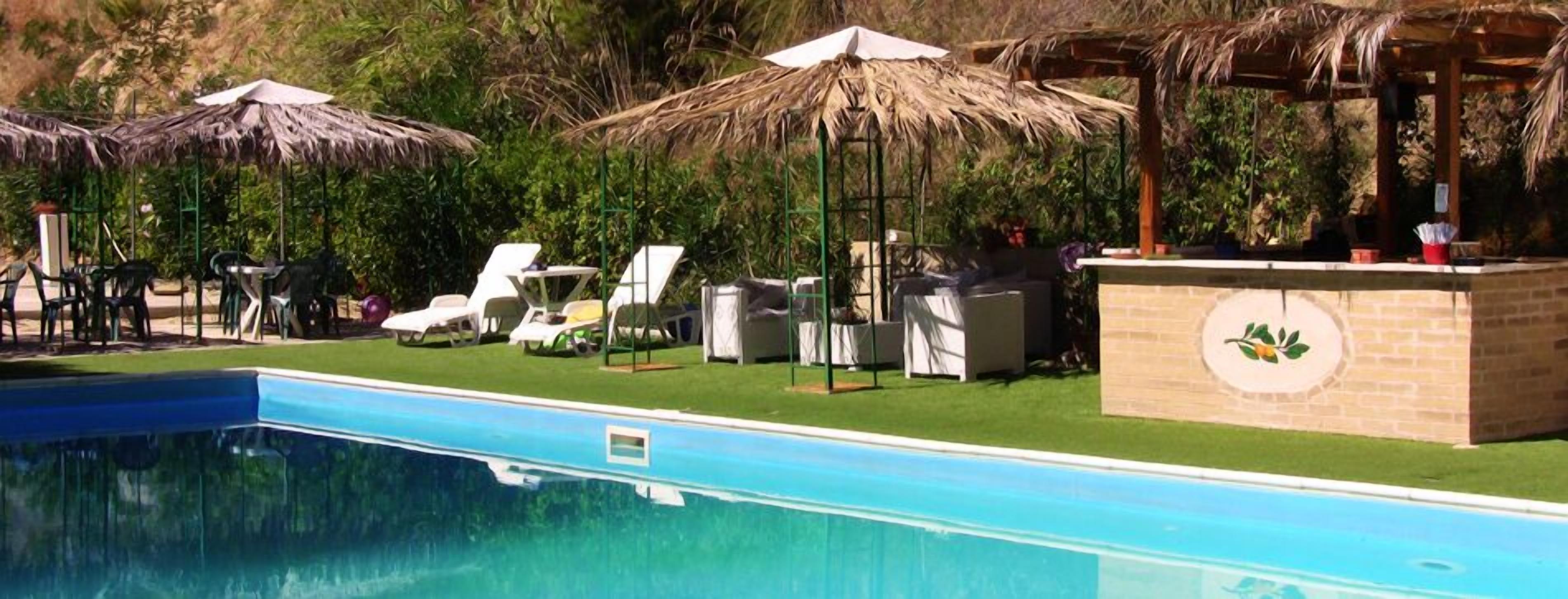 A swimming pool with lounge chairs and umbrellas, surrounded by greenery.