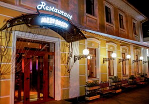 A restaurant with a neon sign, outdoor seating with benches, and a traditional architectural style. - Odesskiy Dvorik (Odesa)