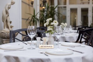 A dining table set with white plates, wine glasses, and a vase with white flowers. A sign on the table reads "RESERVED." - Odesskiy Dvorik (Odesa)