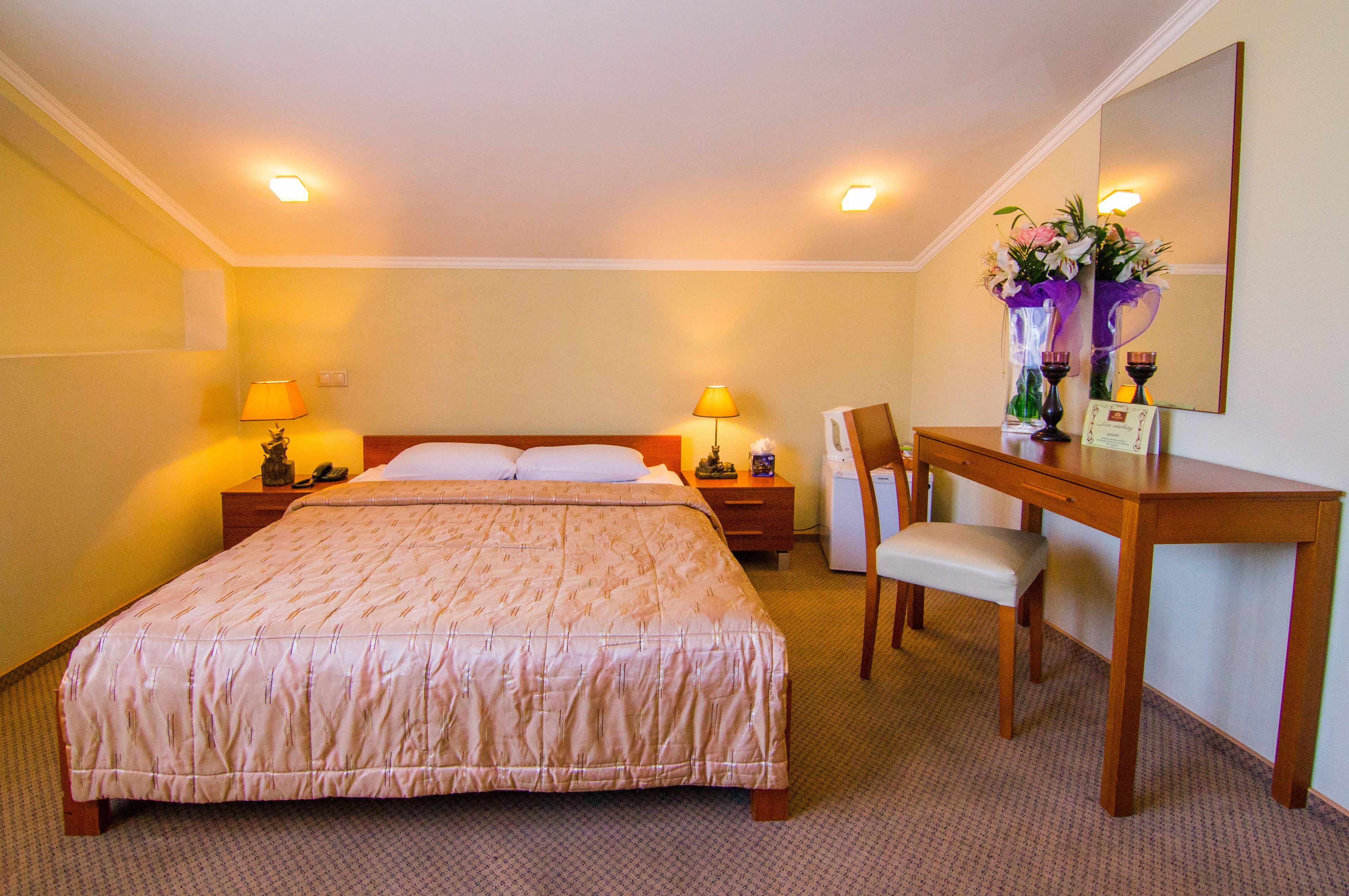 A hotel room with a large bed, bedside lamps, a wooden desk, and a chair.