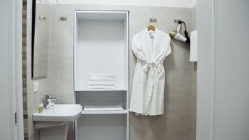 Un baño moderno con ducha integrada, un lavabo y una bata colgada en la pared.
