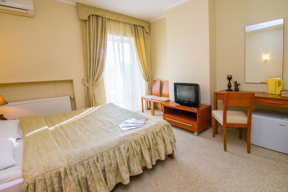 A hotel room with a bed, a desk with a television, a chair, and a small refrigerator.