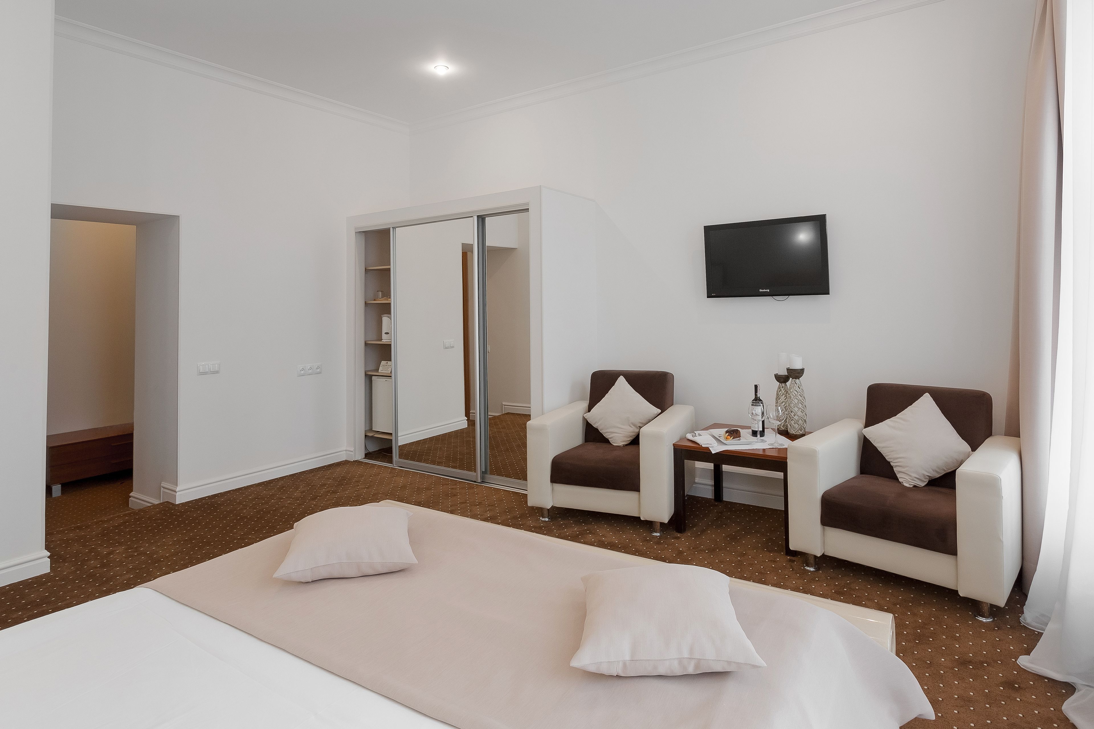 Una habitación de hotel con una cama, dos sillones, un televisor y un espejo.