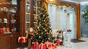 A Christmas tree with gifts, a Christmas stocking, and a Santa Claus figure in a warmly decorated room with a large window and curtains. - Odesskiy Dvorik (Odesa)