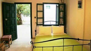 A bedroom with a bed, a wooden stool, and a door leading outside. - Marianna Hotel Apartments (Malevizi)