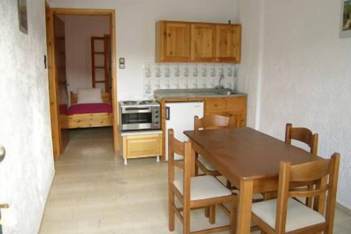Een functionele keuken met houten kastjes, een inbouwoven en een eettafel met stoelen.