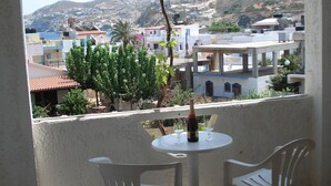 A balcony with two white plastic chairs and a small round table, overlooking a residential area with houses and hills in the background. - Marianna Hotel Apartments (Malevizi)