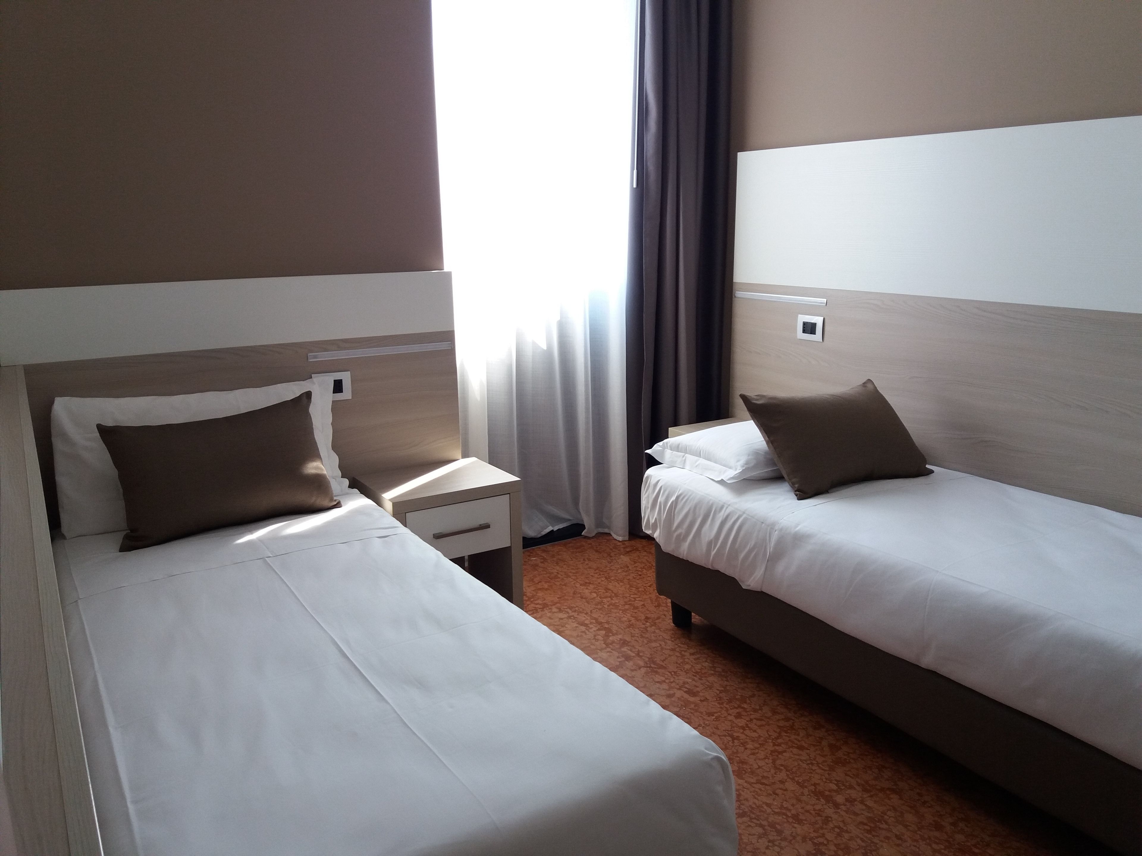 A hotel room with two beds, a nightstand, and a window with curtains.
