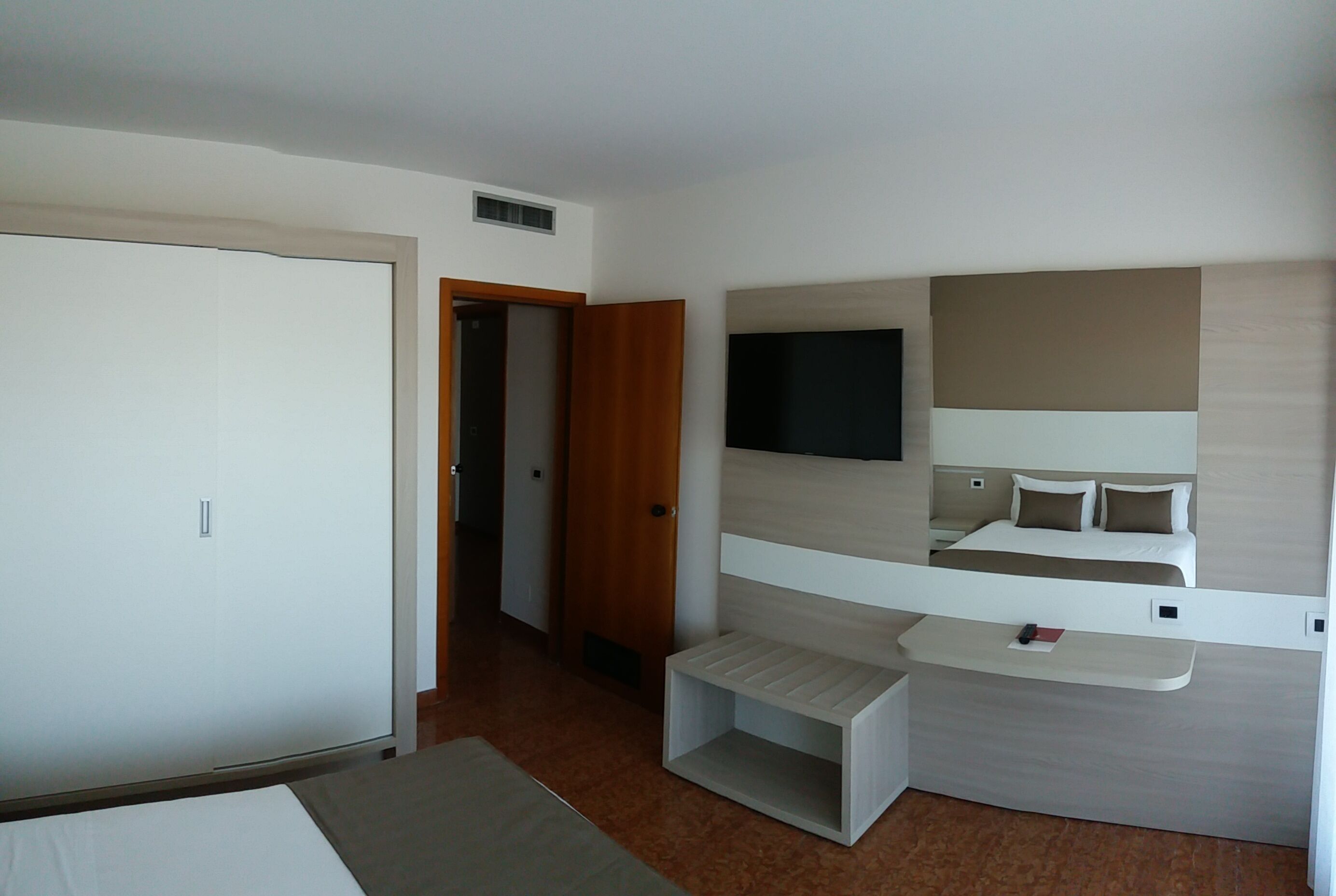A hotel room with a bed, a TV mounted on the wall, a small bedside table, and a wardrobe.