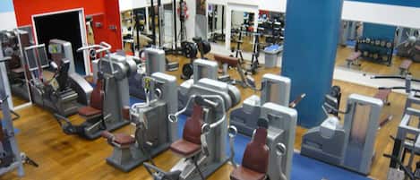 Une salle de sport équipée de divers appareils d’exercice, dotée d’un plancher en bois et arborant une décoration aux couleurs rouge et bleu.