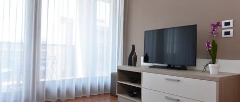 Un salón moderno con un televisor de pantalla plana, un mueble blanco y una orquídea en maceta.