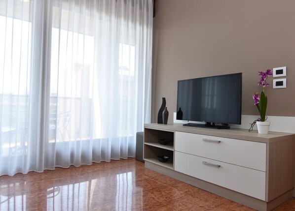 Un salón moderno con un televisor de pantalla plana, un mueble blanco y una orquídea en maceta.