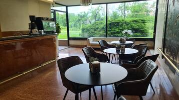 Un intérieur moderne comprenant un espace dédié au café, un coin salon et de grandes fenêtres offrant une vue sur la verdure.