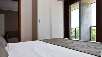 A bedroom with a bed, a wardrobe, and a balcony with a view.