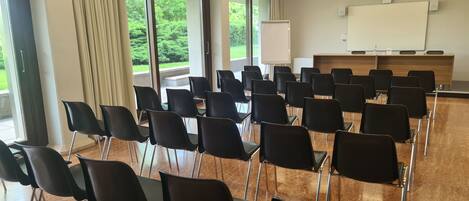 A conference room with rows of black chairs, a whiteboard, and a projector screen.