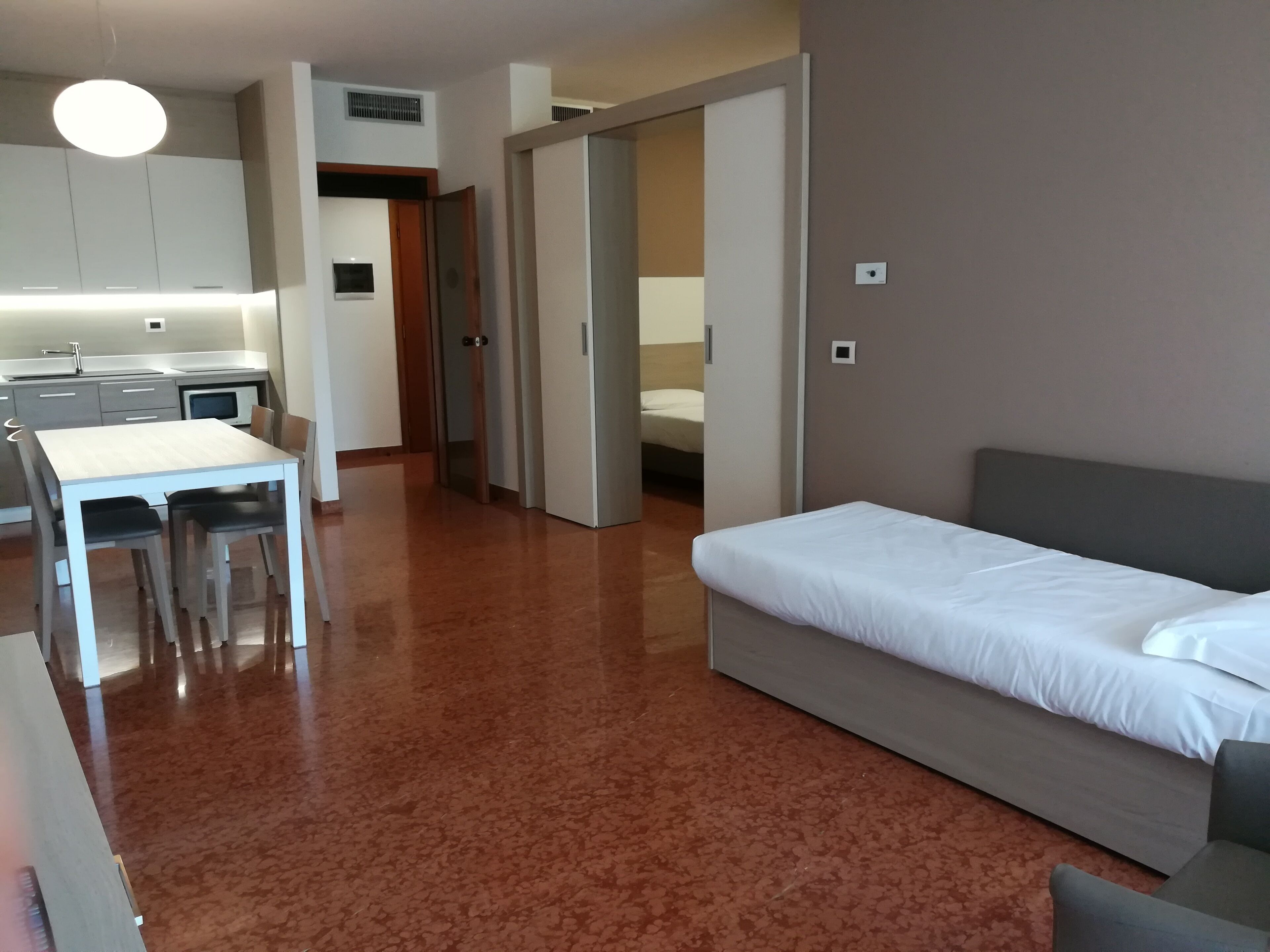 Habitación de hotel con cama, una pequeña mesa con sillas, kitchenette y baño visible a través de una puerta abierta.