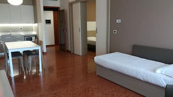 A hotel room with a bed, a small table with chairs, a kitchenette, and a bathroom visible through an open door.
