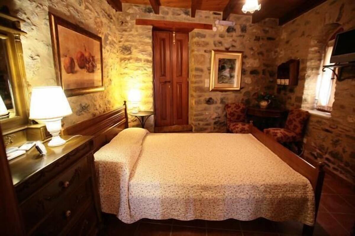 A rustic room with a bed, wooden dresser, and stone walls.