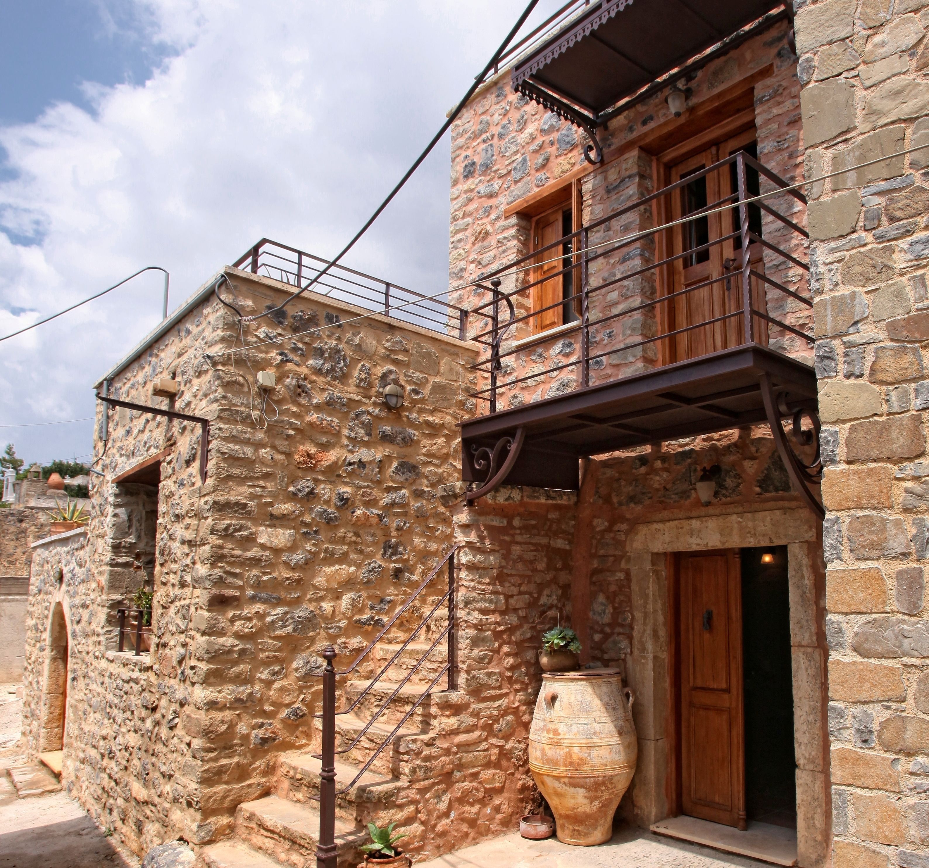 Un edificio de piedra con puerta de madera, un balcón y una maceta grande afuera.