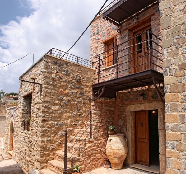 A stone building with a wooden door, a balcony, and a large pot outside. - Dorovinis Country Houses (Ierapetra)