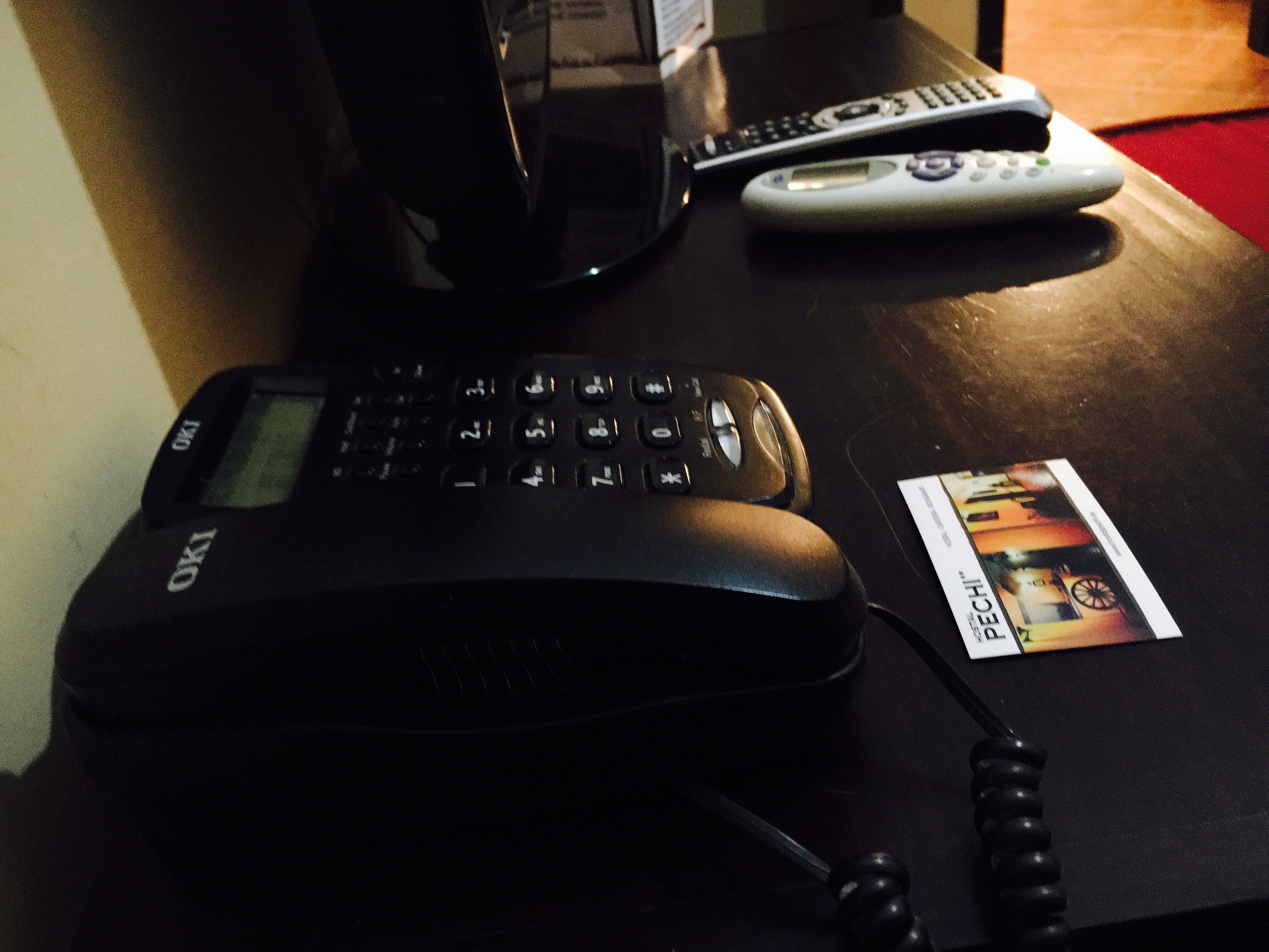 A black office phone, two remote controls, and a business card on a wooden table.