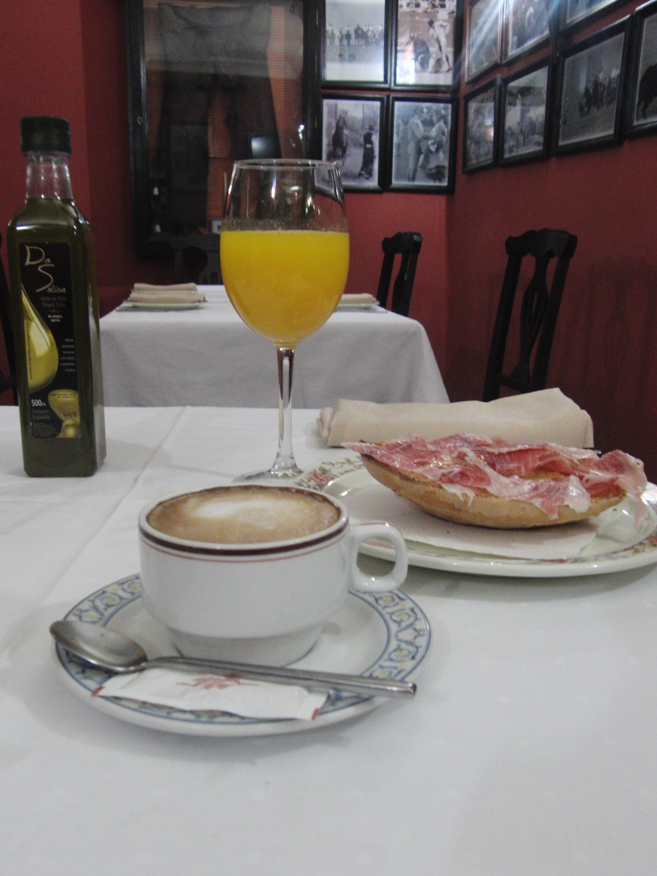 Une table avec une tasse de café, un verre de jus d’orange et une assiette avec un sandwich.