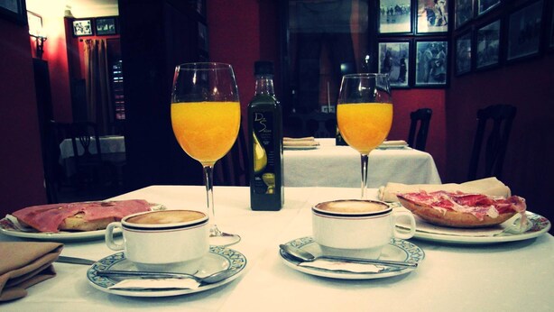 A dining table with two cups of coffee, two glasses of orange juice, and plates of food including a sandwich and a pastry. - Hostal Pechi (Huevar del Aljarafe)