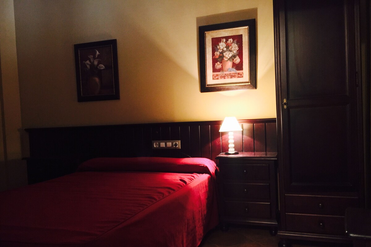 A hotel room with a bed, a nightstand with a lamp, a dresser, and two framed pictures on the wall.