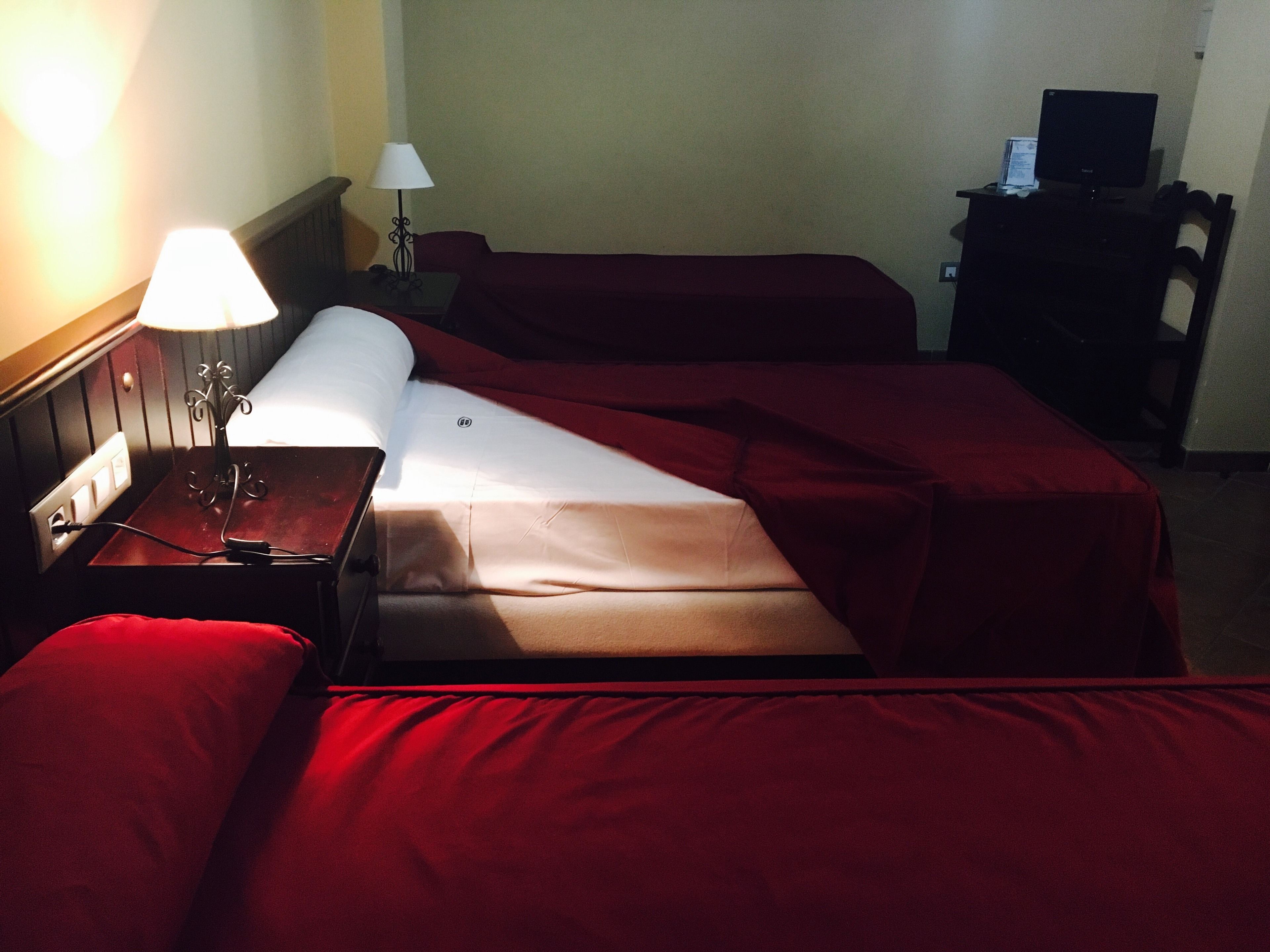 Habitación de hotel con dos camas, un escritorio con lámpara, una silla y televisor.