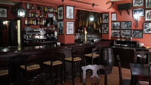 A bar area with wooden chairs, a bar counter, and shelves of bottles. - Hostal Pechi (Huevar del Aljarafe)