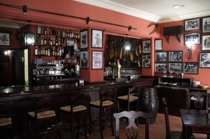 Una zona de bar con sillas de madera, una barra y estantes llenos de botellas.