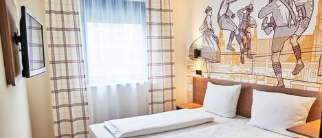 A hotel room with a bed, a TV mounted on the wall, and a large window with curtains.