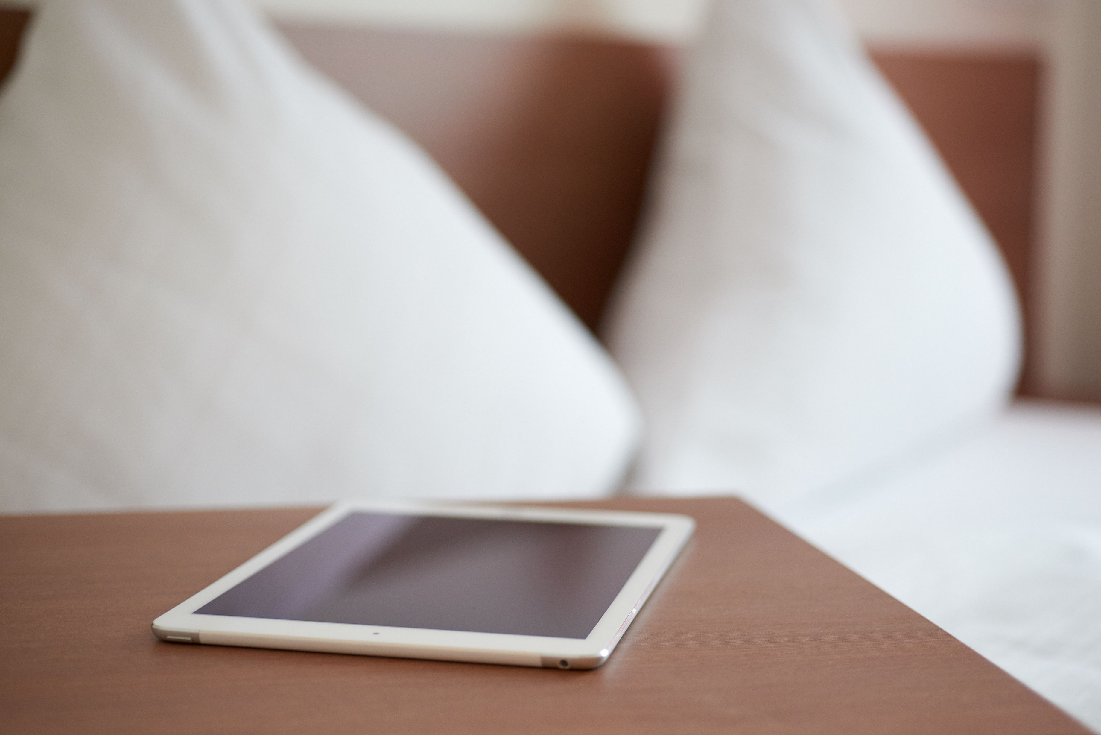 A tablet on a wooden table in a room with a brown couch and white pillows.