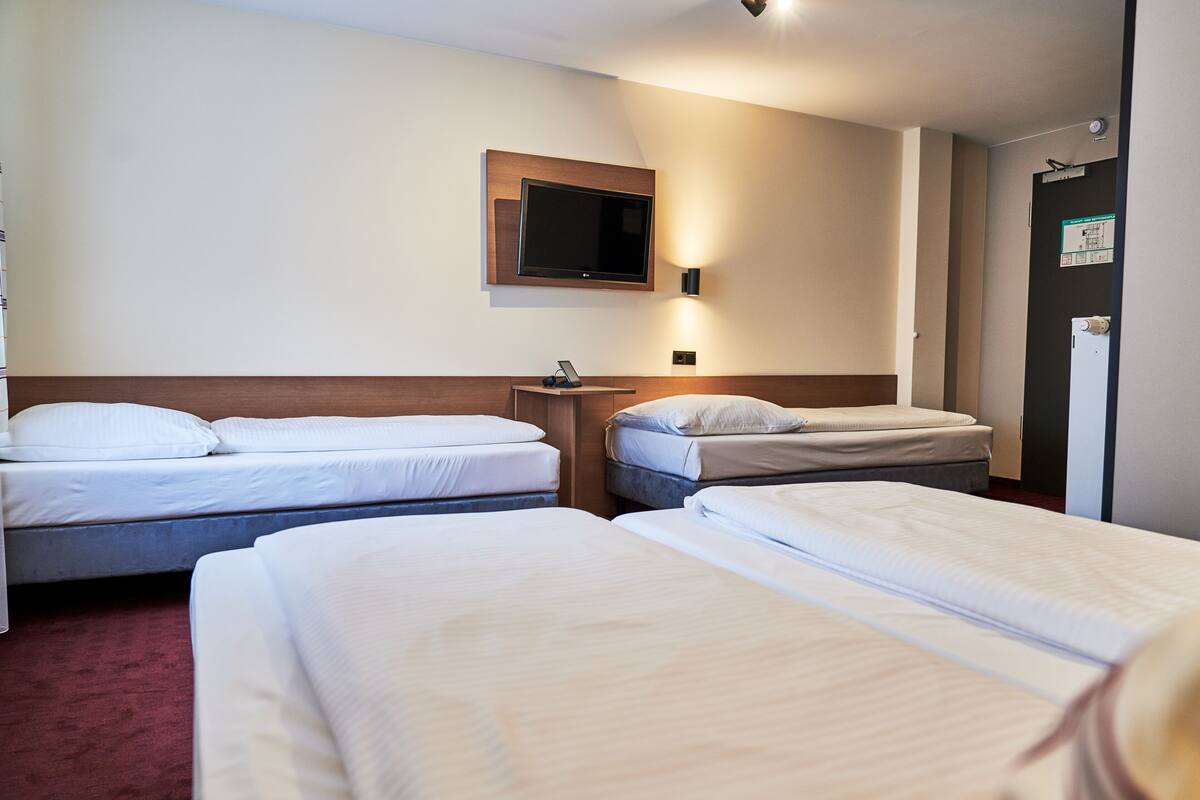A hotel room with two single beds, a mounted TV, a bedside table, and a door with a sign.