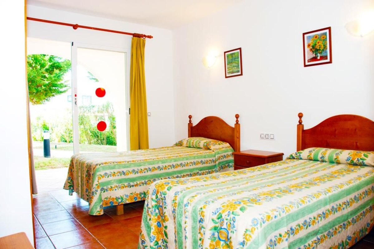 Une chambre avec deux lits, une fenêtre avec des rideaux, une porte et un mur orné d’un tableau.