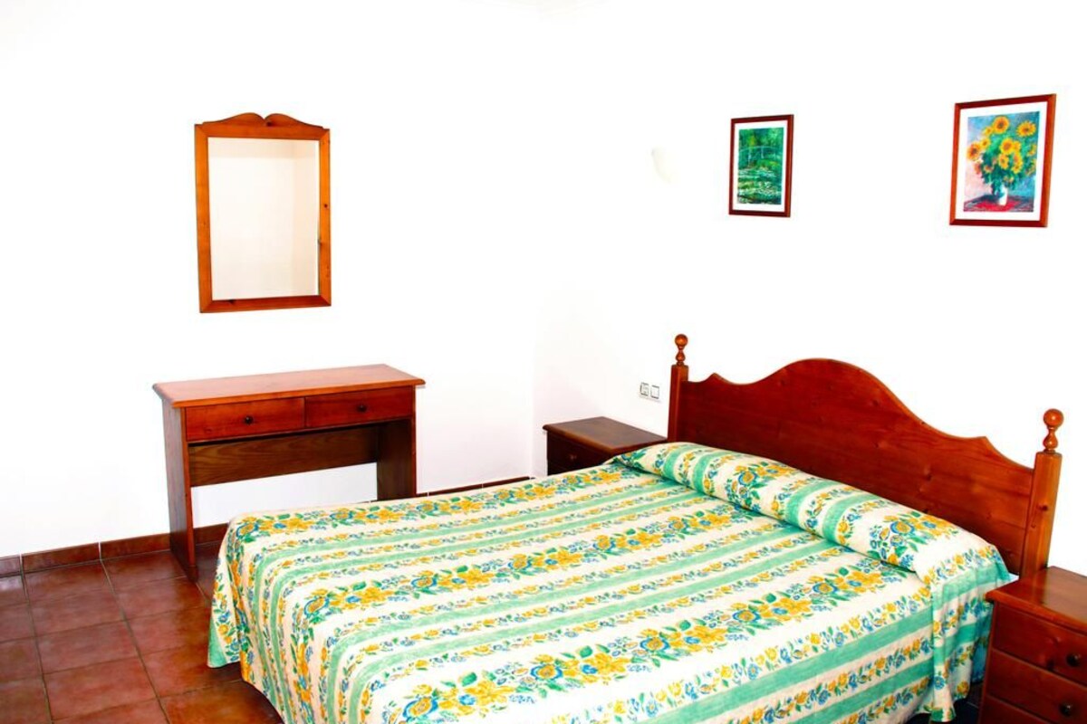 Un dormitorio con una cama de madera, una mesita de noche, un aparador y un espejo en la pared.