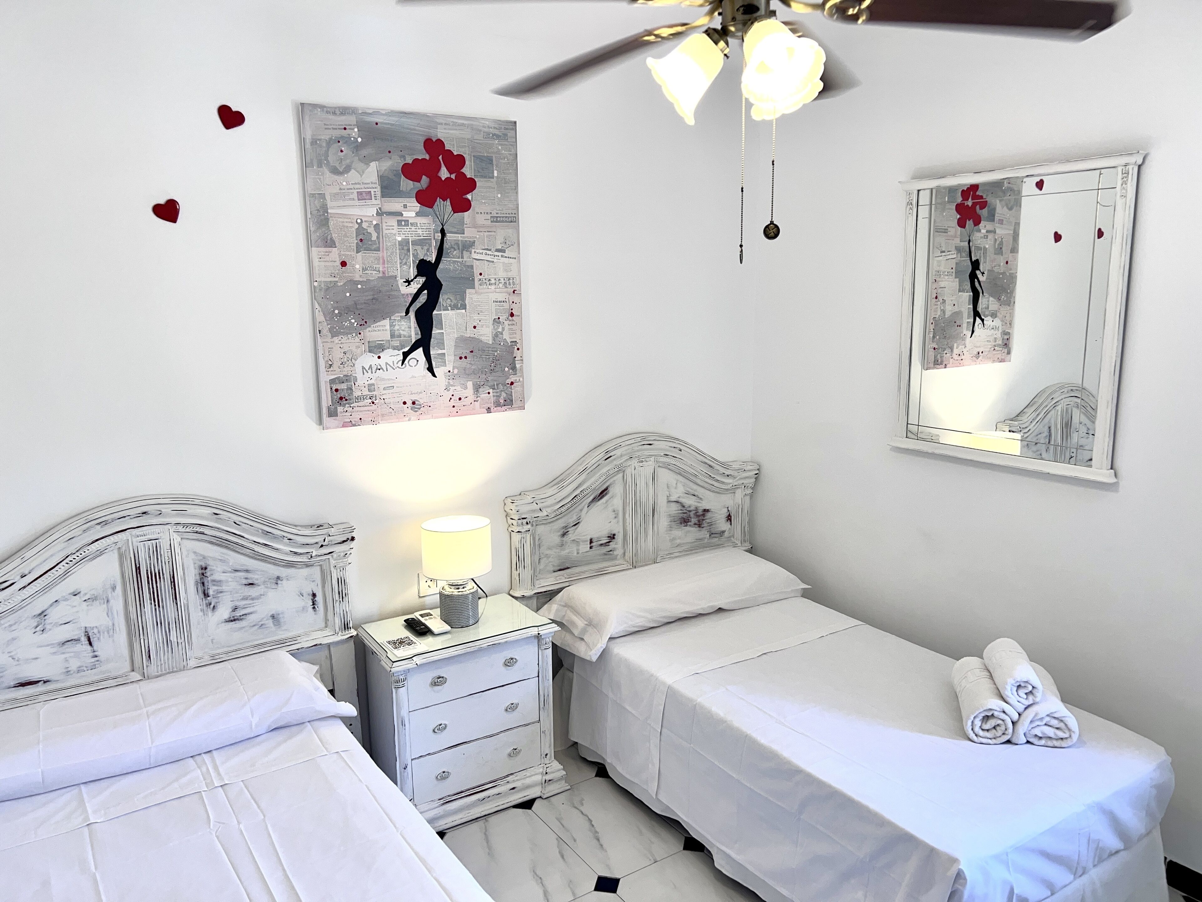A bedroom with two beds, a nightstand with a lamp, and artwork on the walls.