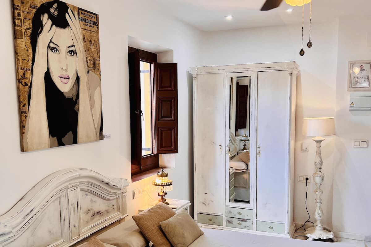 A bedroom with a large bed, a ceiling fan, a wardrobe, and a painting on the wall.