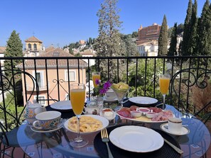 Mesa posta com comida e bebidas numa varanda com vista para uma cidade.