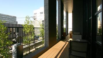 A balcony with a view of a cityscape, featuring a statue, potted plants, and a table with chairs.