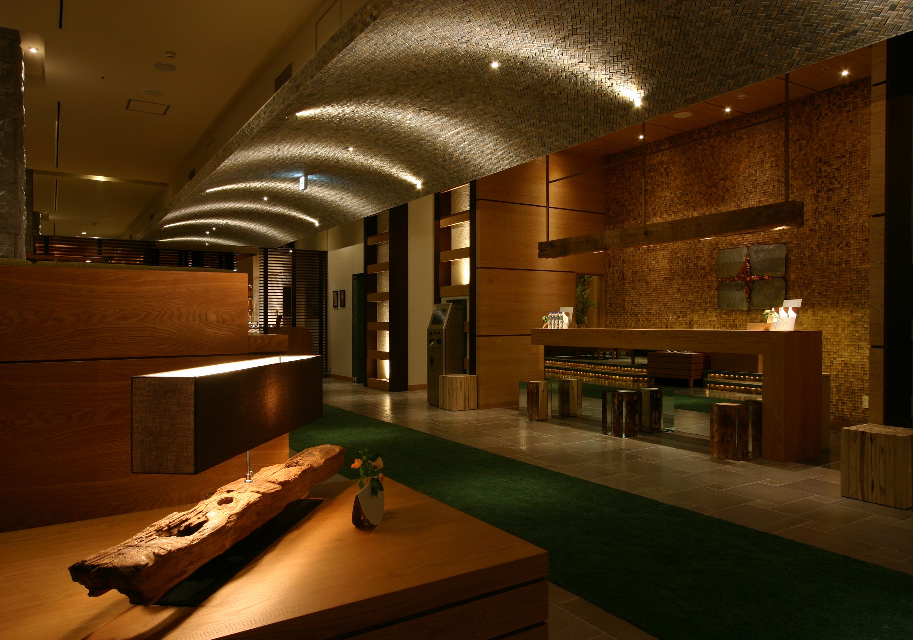 Un vestíbulo moderno con mostrador de recepción, zona de recepción de madera y área de bar con taburetes.